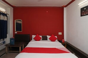 A hotel room with a bed, a nightstand, a mirror, a red wall, and a window with curtains.