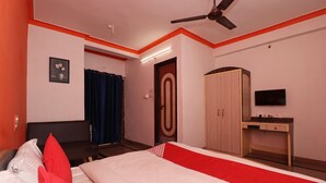 Quarto de hotel com cama, guarda-roupa, escrivaninha e televisão.