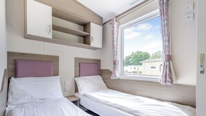 Een slaapkamer met twee bedden, inbouwplanken, een raam met gordijnen en uitzicht op buiten.