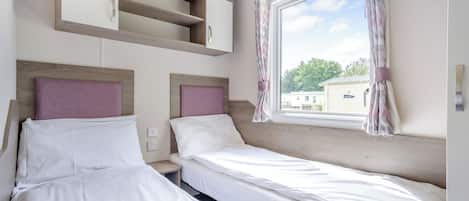 A bedroom with two beds, built-in shelves, a window with curtains, and a view of the outside.