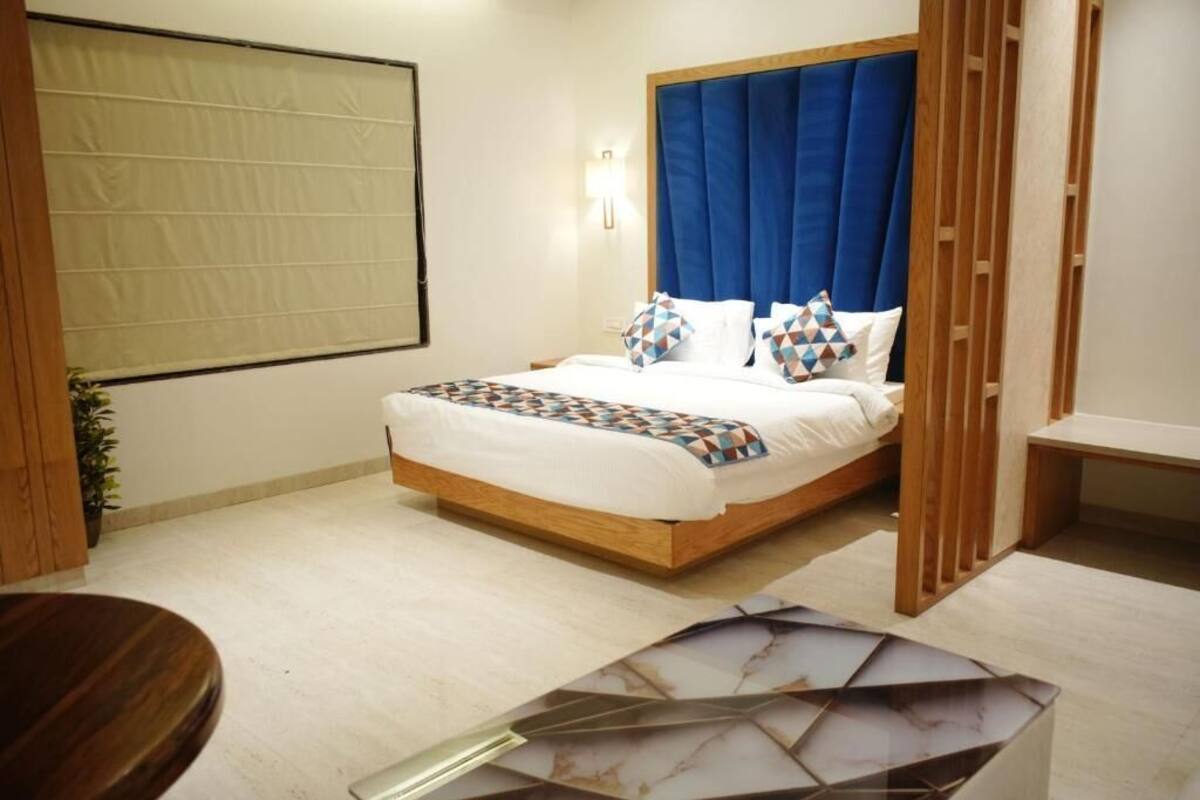 A bedroom with a bed, a bedside table, a nightstand, a window with curtains, and a potted plant.