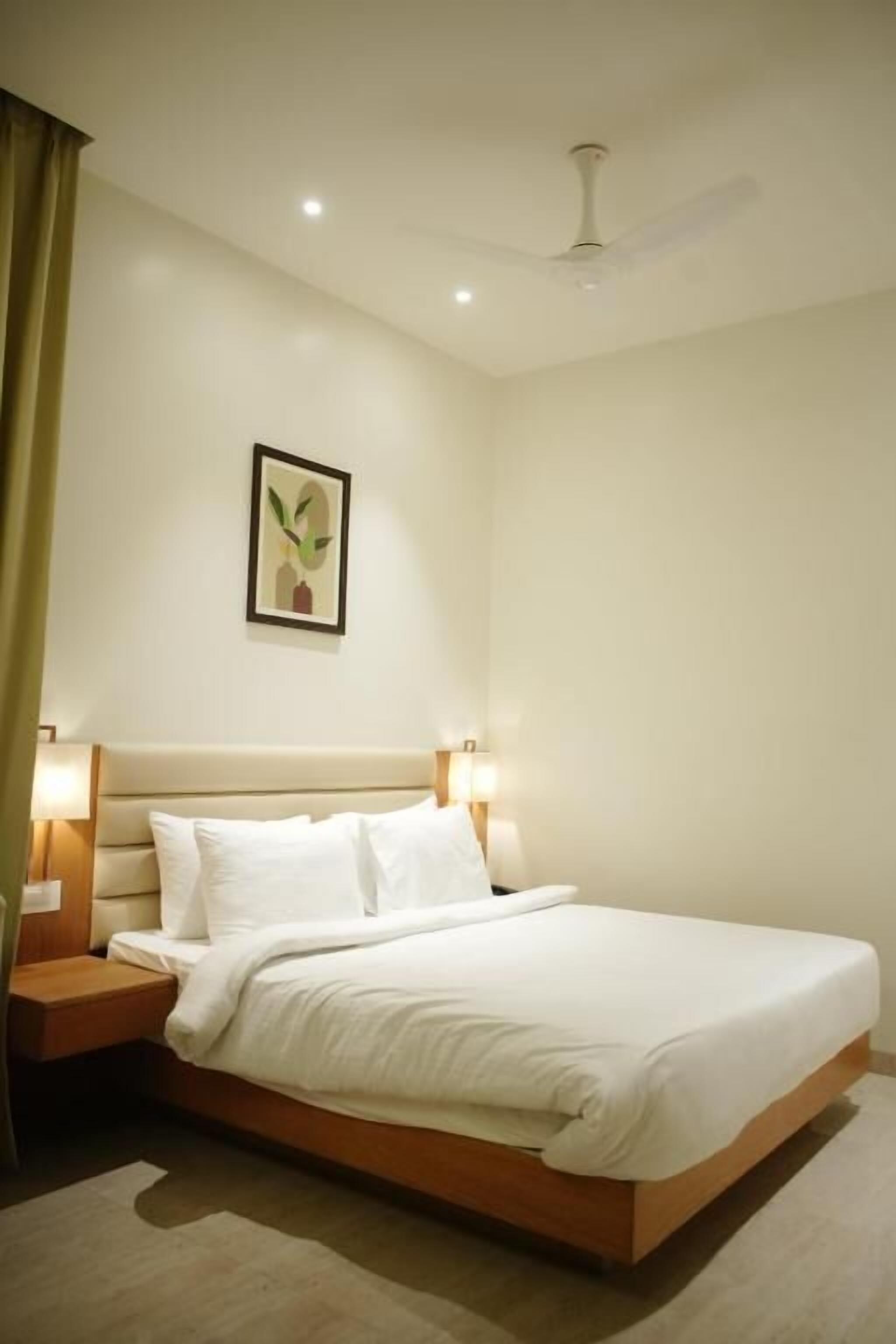 A neatly made bed in a hotel room with a headboard, bedside lamps, and a ceiling fan.