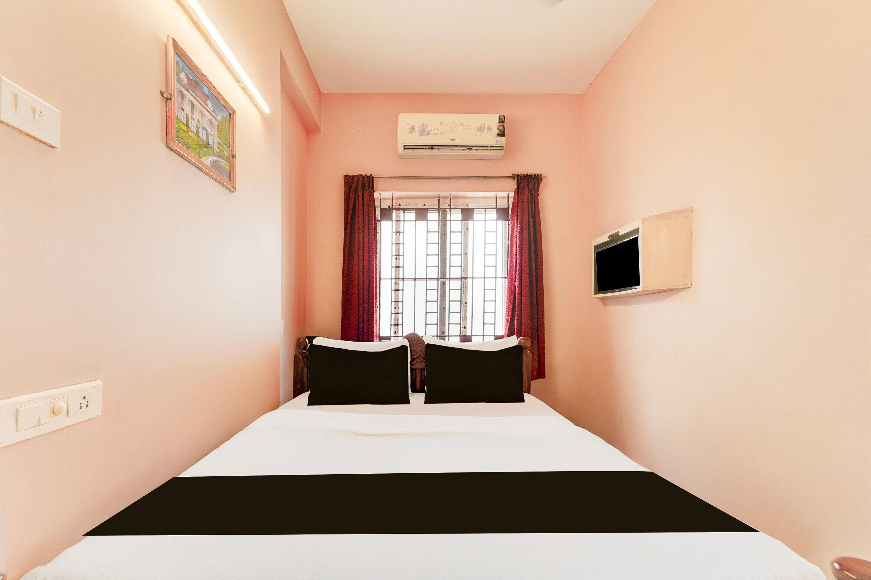 A bedroom with a bed, a TV, an air conditioner, a window with curtains, and a painting on the wall.
