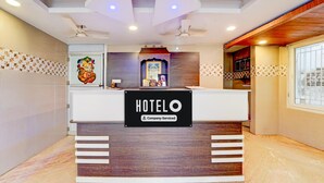 Un comptoir d’accueil d’hôtel avec une enseigne « HOTELO », des ventilateurs de plafond et un tableau encadré au-dessus du comptoir.
