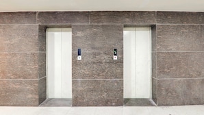 Two elevators with control panels, set in a modern building with a stone facade. - Deluxe Civil Lines Near Old Bus Stand Imperial (Bareilly)