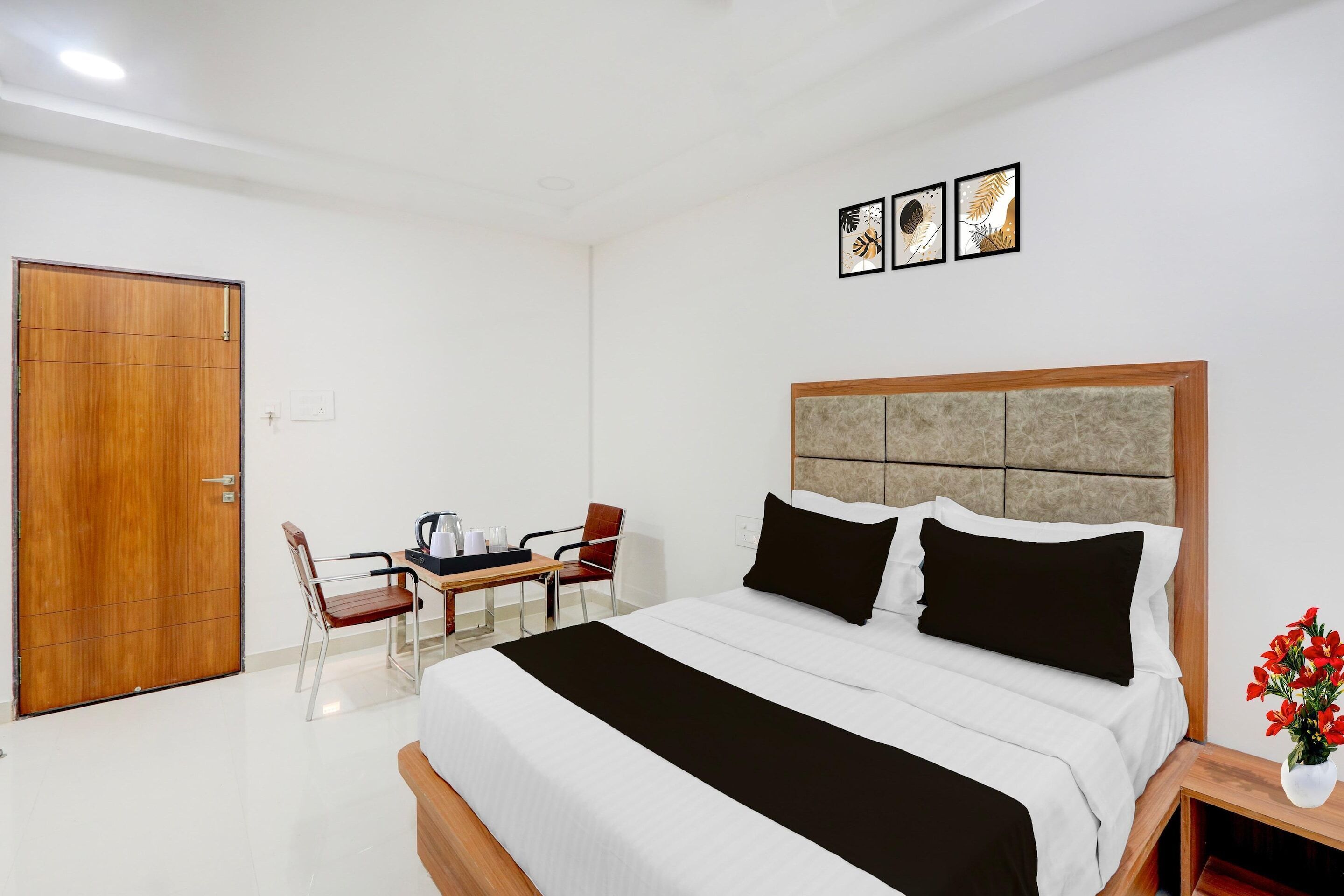 A hotel room with a bed, a desk, a chair, a wooden door, and framed artwork on the wall.