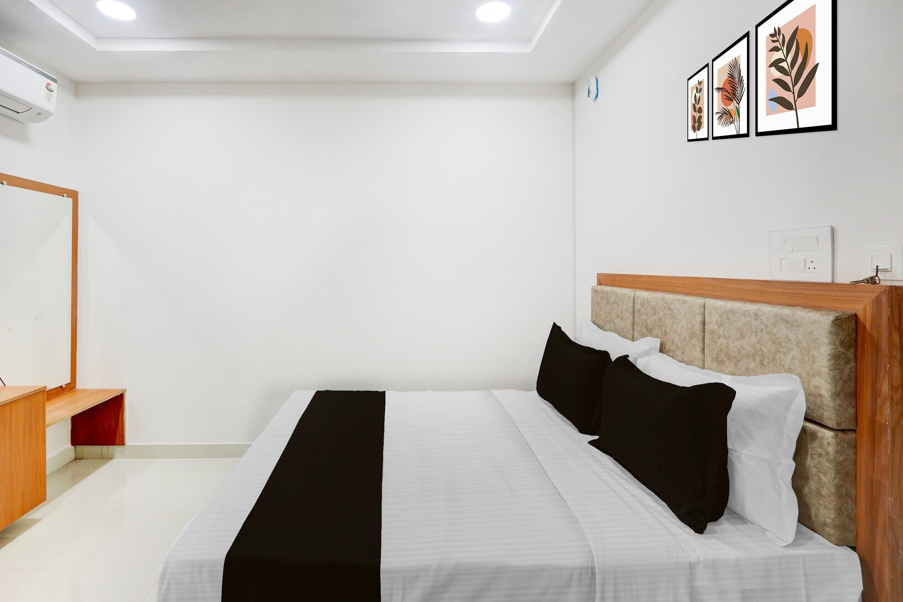 Ein Hotelzimmer mit Bett, Schreibtisch aus Holz, Wandairconditioner und gerahmten Kunstwerken.