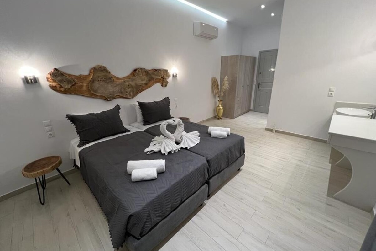 Ein modernes Hotelzimmer mit einem großen Bett, einem runden Holfnachtkästchen, einer Wandleuchte und einem großen dekorativen Element über dem Bett.