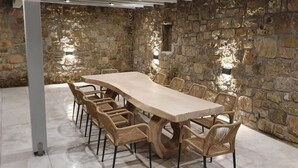 Een kamer met stenen muren, een lange houten tafel en rieten stoelen.