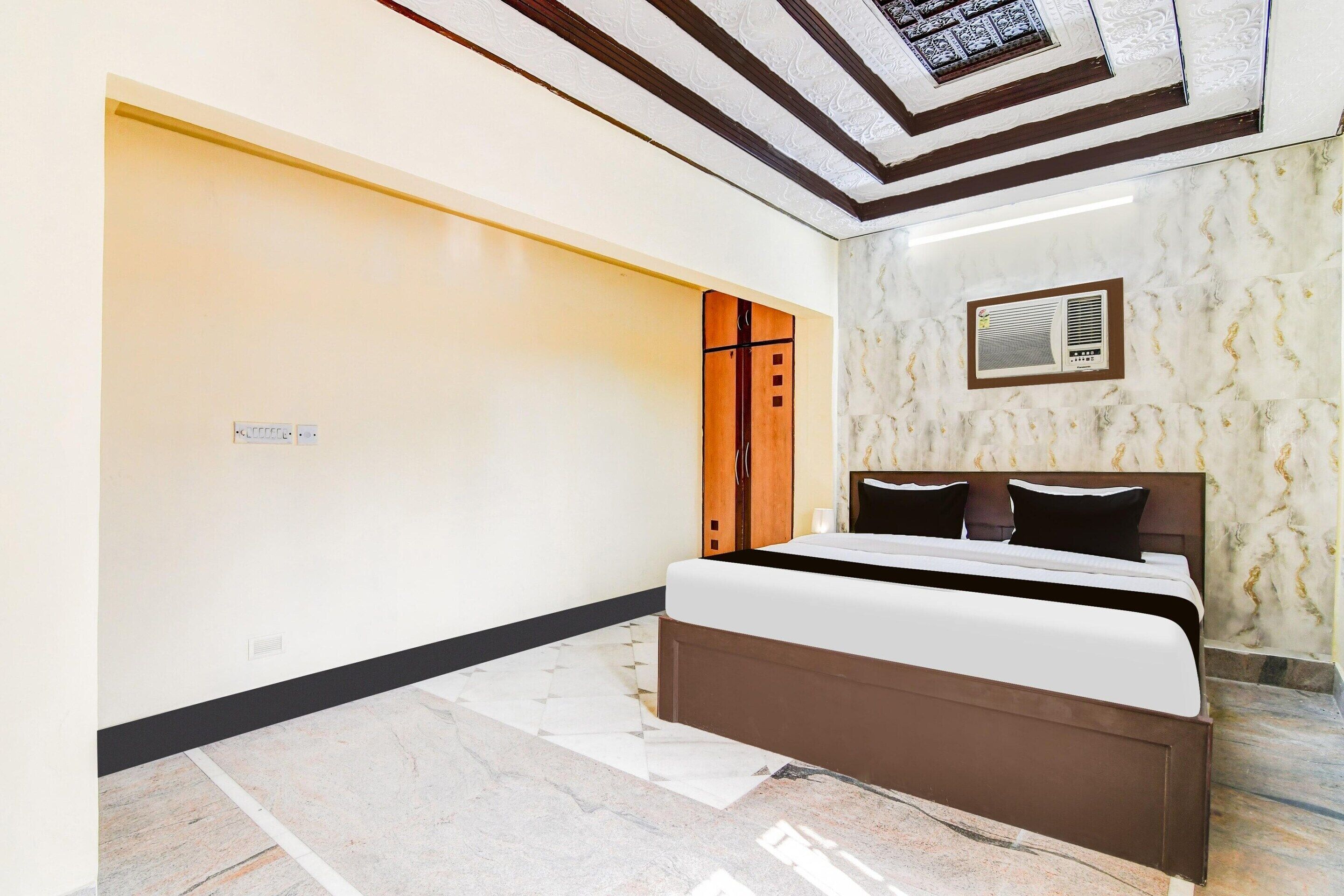A bedroom with a bed, a wardrobe, a ceiling with a patterned design, and a wall-mounted air conditioning unit.