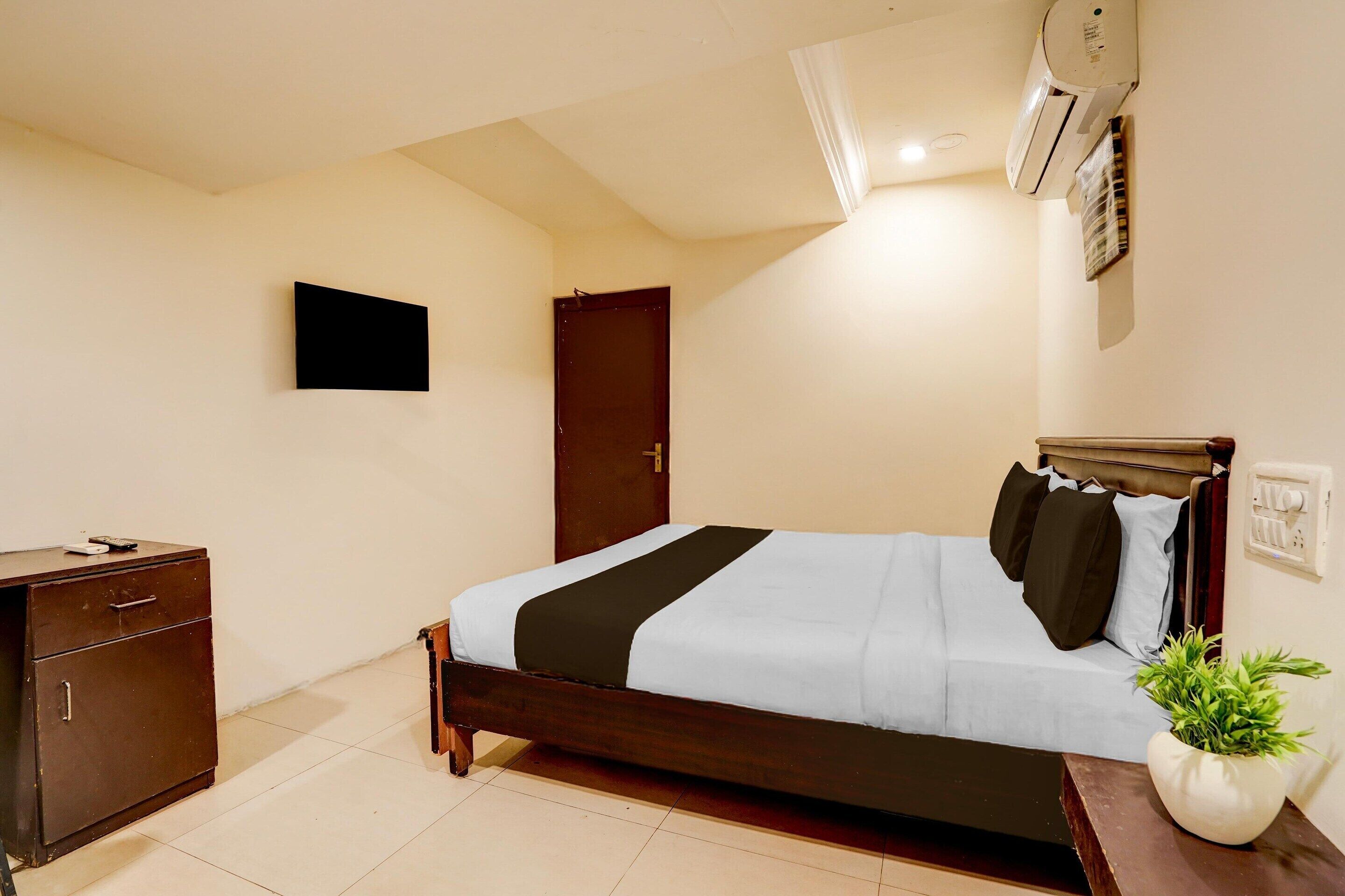 A bedroom with a bed, a dresser, a potted plant, and an air conditioning unit.
