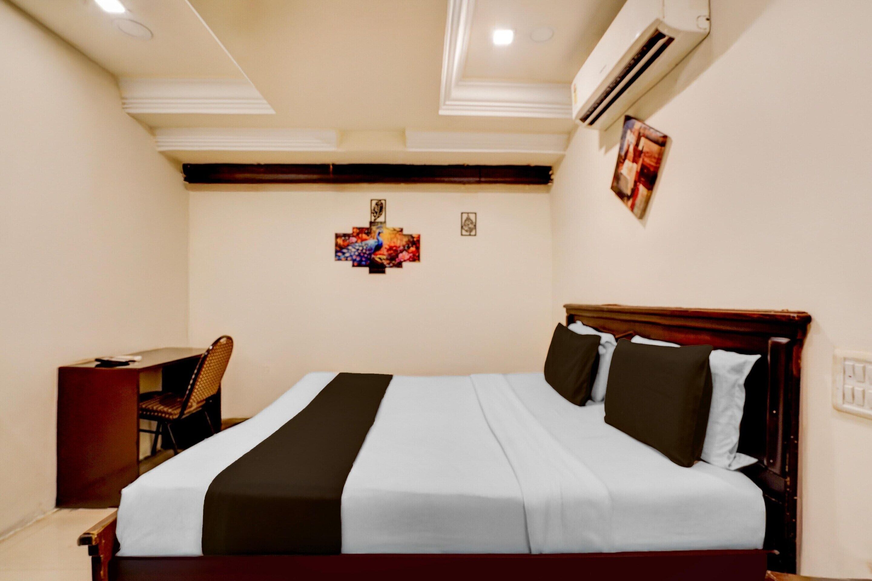A hotel room with a bed, a desk, a chair, and a wall-mounted air conditioner.