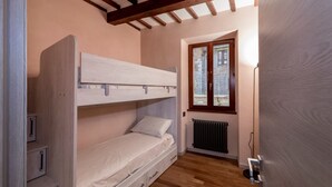 Une petite pièce, de taille modeste, comprenant un lit superposé, un radiateur et une fenêtre donnant sur un paysage agréable.