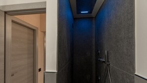 Une petite salle de douche aux couleurs sombres, avec une pomme de douche et un panneau de commande bien visibles.