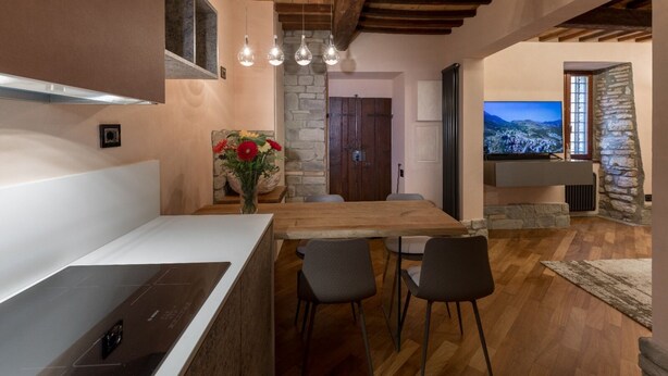 Une cuisine moderne avec une table en bois, des tabourets de bar, un mur en pierre et un téléviseur fixé au mur.