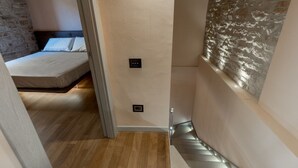 Un couloir étroit avec un lit, une lampe fixée au mur et un mur à texture.