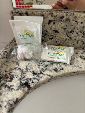Encimera de granito con una bolsa de champú Mahle Comfort Hotel, una pastilla de jabón y una botella de plástico.