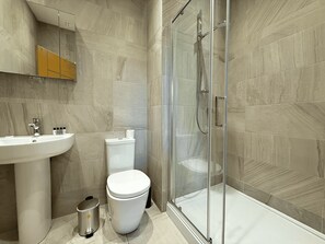 Ein Badezimmer mit einer Duschkabine, einem Waschbecken, einer Toilette und einem Mülleimer.