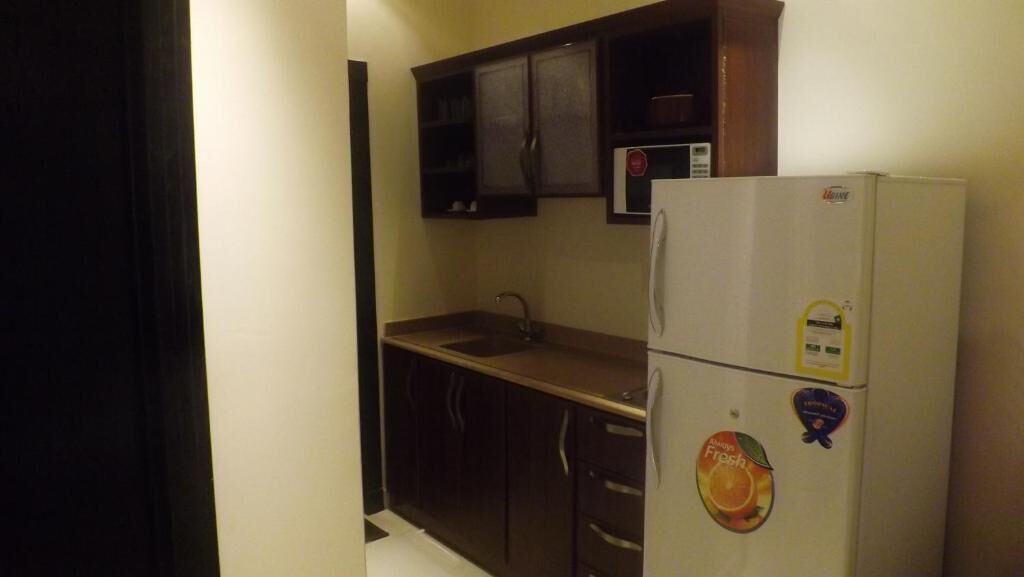 A compact kitchen with dark cabinets, a white refrigerator, and a microwave.