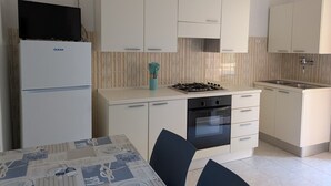 A compact kitchen with white cabinets, a gas stove, a built-in oven, and a refrigerator. - Caorle ground floor property near the sea (Caorle)