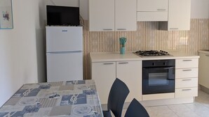 A compact kitchen with a refrigerator, stove, oven, and a dining table with chairs. - Caorle ground floor property near the sea (Caorle)