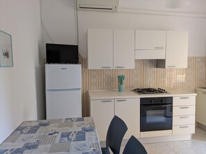 Eine kleine Küche mit Kühlschrank, Herd, Backofen und einem Esstisch mit Stühlen.