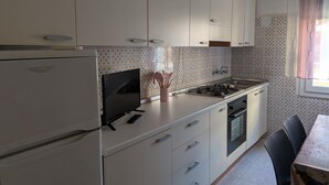 Una cocina con armarios blancos, estufa, refrigerador y televisor.