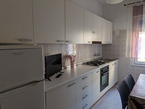 Eine Küche mit weißen Schränken, einem Herd, einem Kühlschrank und einem Fernseher.