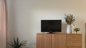 Et træmøbel til TV med et fladskærms TV, to potteplanter og en vase med tørrede blomster.