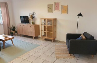 A living room with a sofa, a TV on a wooden cabinet, a glass cabinet with wine glasses, and a floor lamp.