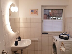 Ett badrum med handfat, spegel, fönster och tvättmaskin.