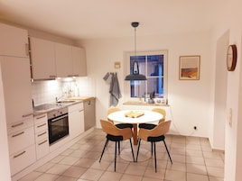A modern kitchen with white cabinets, a built-in oven, a dining table with four chairs, and a window with a view of a building.