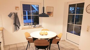 En spiseplads med et rundt bord, fire stole, en pendel og et vindue med udsigt.