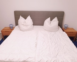 A bed with a grey headboard, two white pillows, and a white duvet. There are two bedside tables with lamps.