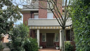Een tweelaags bakstenen gebouw met een voortuin, wenteltrap naar de ingang en een verzorgd gazon.