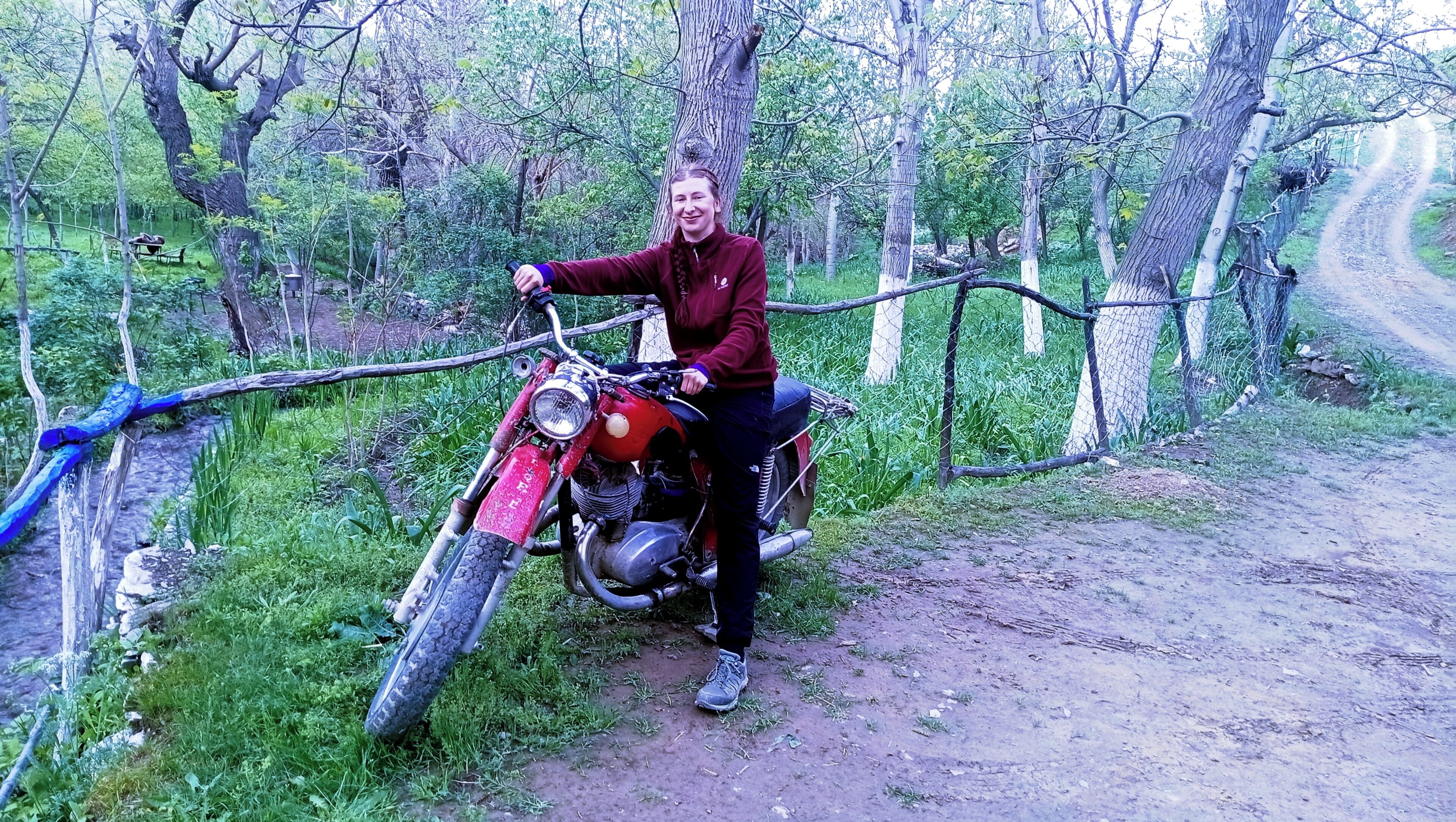 Uma pessoa sentada em uma motocicleta em área arborizada com trilha de terra.