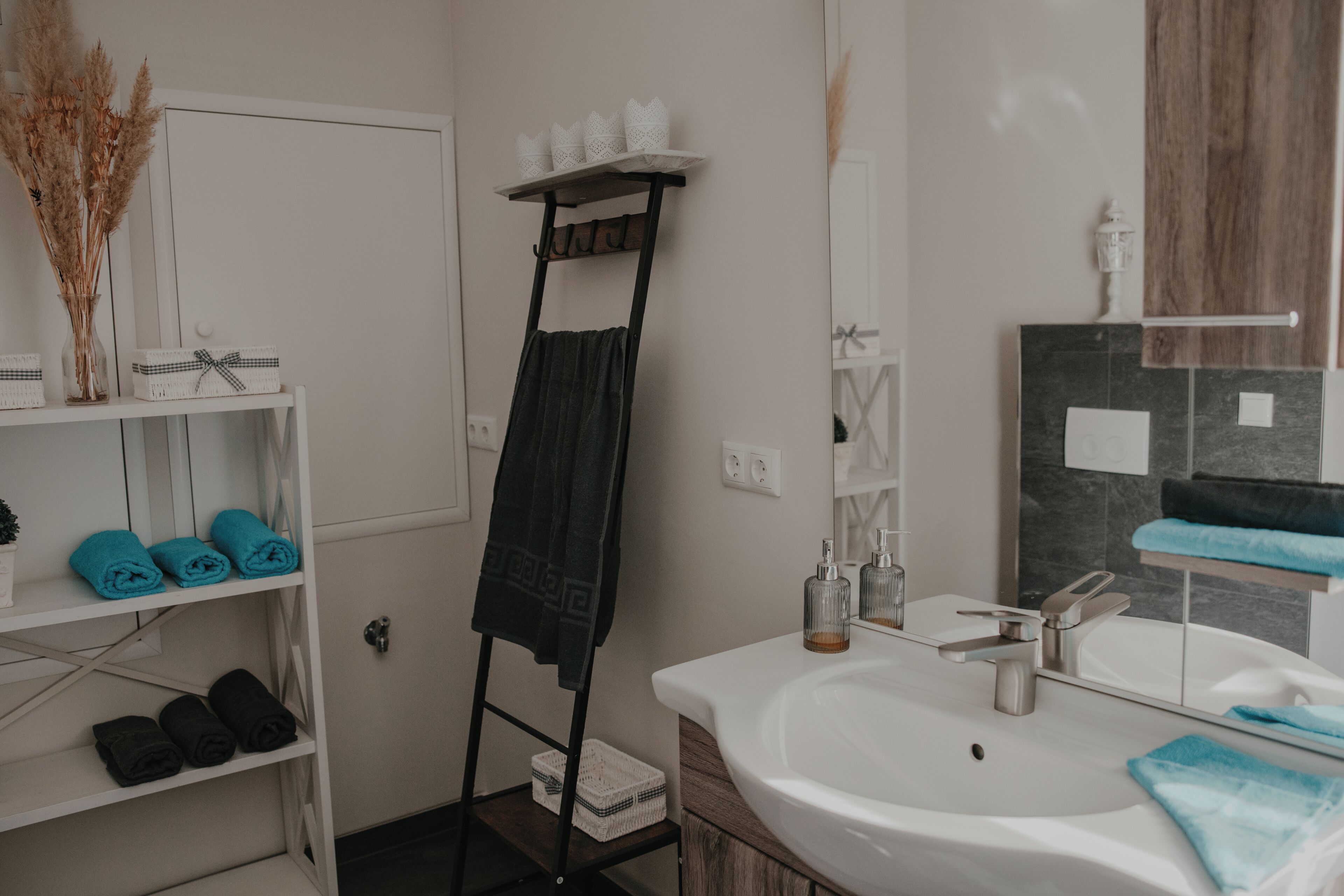 A bathroom with a white sink, a mirror, a towel rack, and shelves with towels.