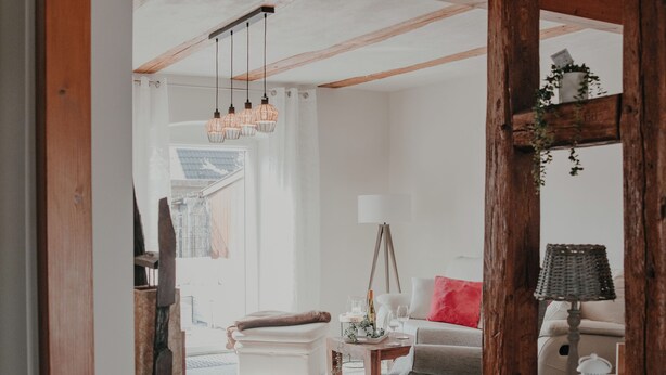 A room with wooden beams, a white ceiling, a red cushion, a wicker basket, and a white lantern. - Villa Gänseblümchen—Vacation Home Near Schwerin, Accessible (Brüsewitz)