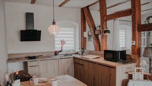 A modern kitchen with wooden beams, a flat-screen TV, and a dining area with a table set for two. - Villa Gänseblümchen—Vacation Home Near Schwerin, Accessible (Brüsewitz)