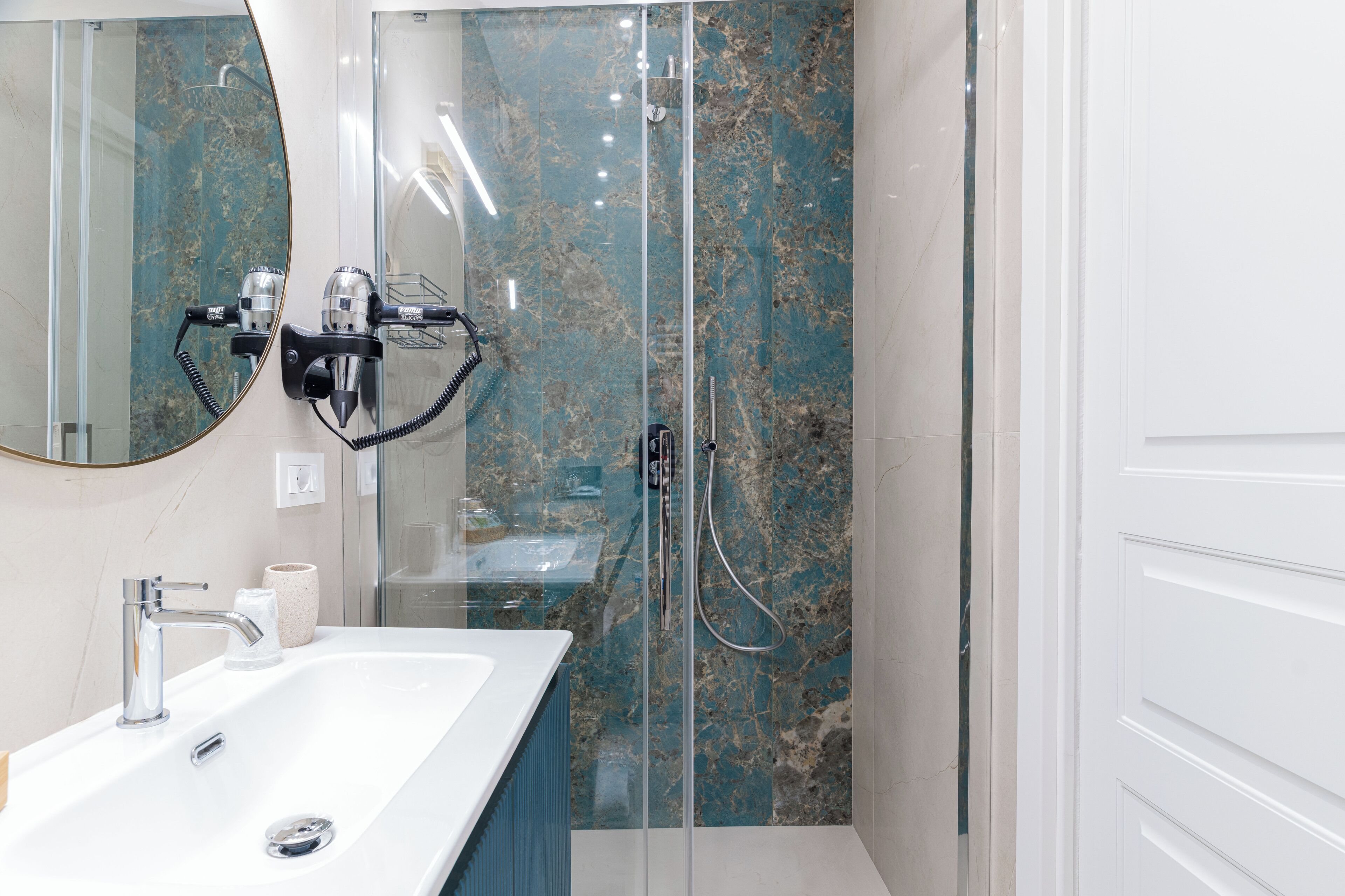 Une salle de bain avec un lavabo blanc, un grand miroir et une douche séparée par des parois en verre.