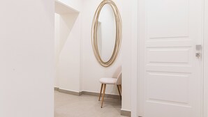 A hallway with a white door, a white chair, and a gold-framed mirror on the wall. - Nimbus Rooms (Naples)