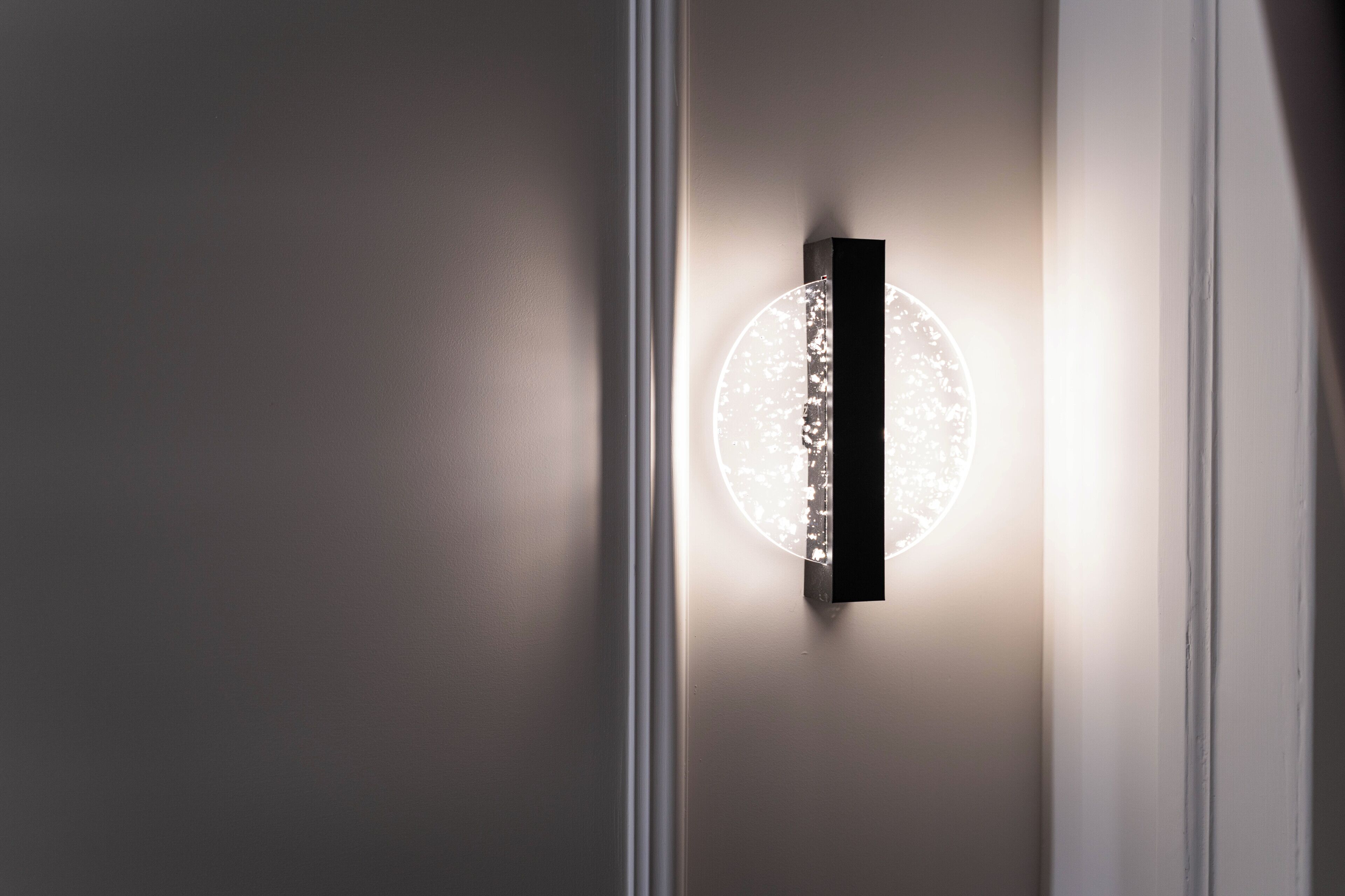 A wall-mounted light fixture with a circular design and a rectangular base.