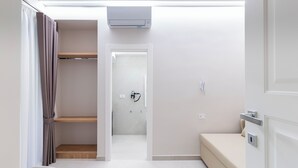 A modern, minimalistic room with a bed, a chair, a wardrobe, and a shower area. - Nimbus Rooms (Naples)