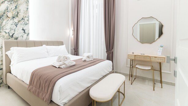 A hotel room with a bed, a bedside table, a chair, a mirror, and a wall with a marble-like pattern. - Nimbus Rooms (Naples)