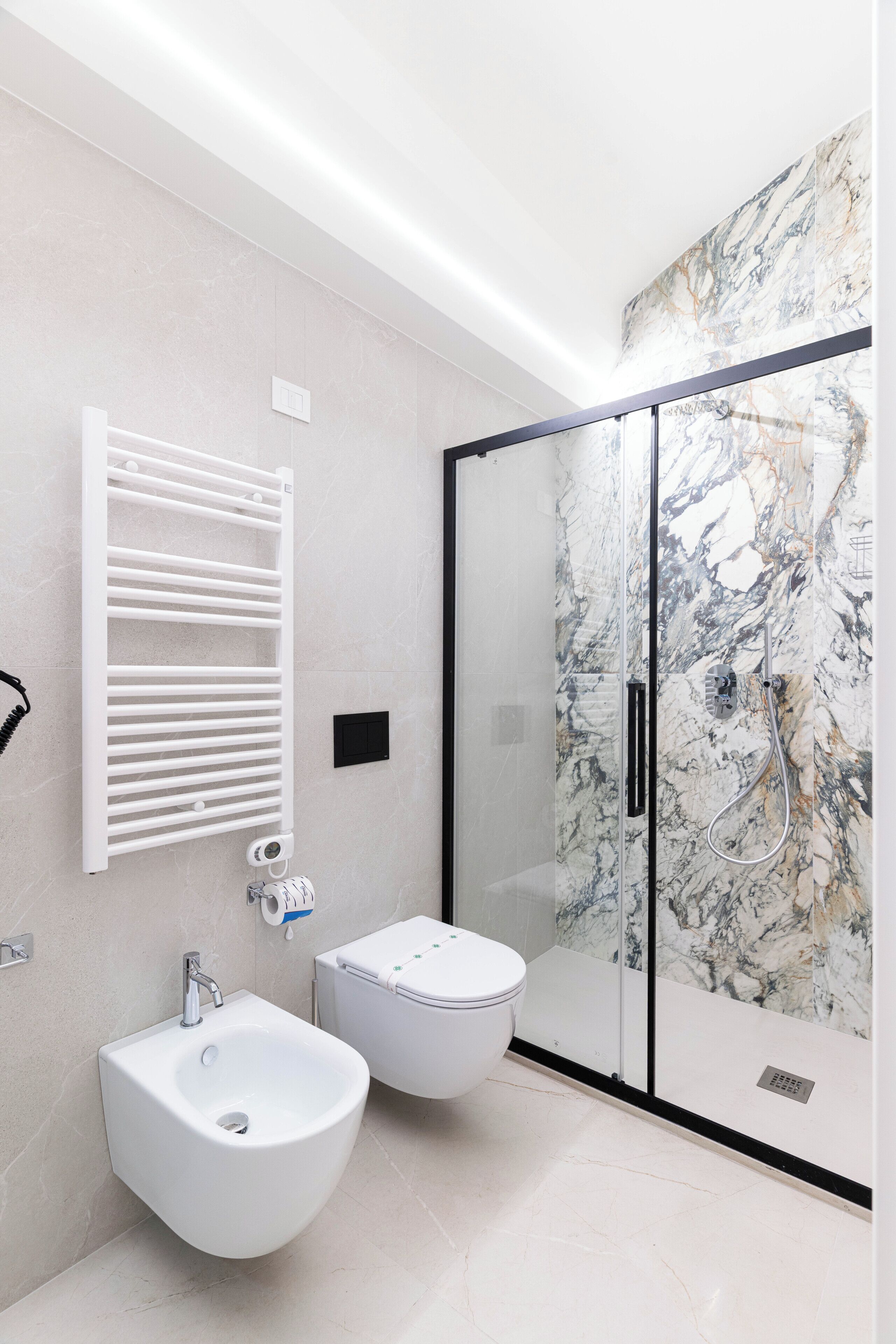 A modern bathroom with a bidet, a glass shower enclosure, and a marble wall.