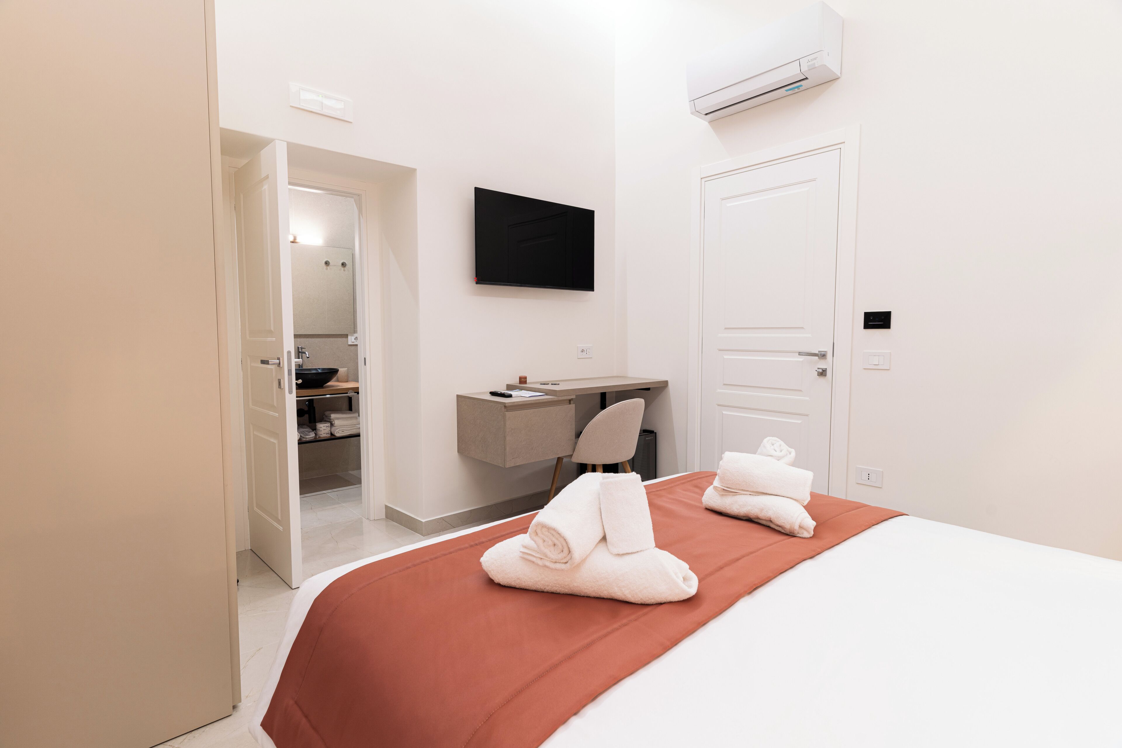 A hotel room with a bed, a desk, a chair, and an air conditioning unit.