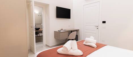 A hotel room with a bed, a desk, a chair, and an air conditioning unit.