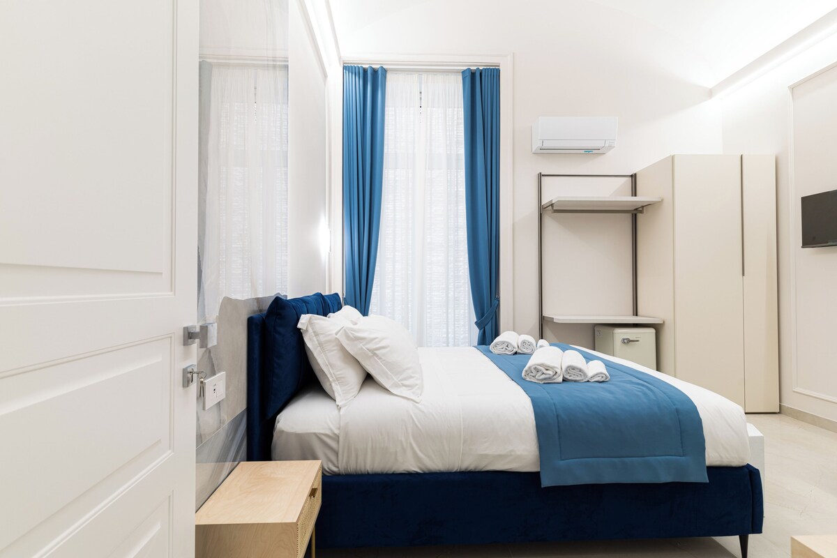 Une chambre d’hôtel avec un lit, une table de chevet, une armoire, un miroir et une fenêtre avec des rideaux.