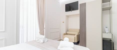 A hotel room with a bed, a chair, a TV, and a minibar.
