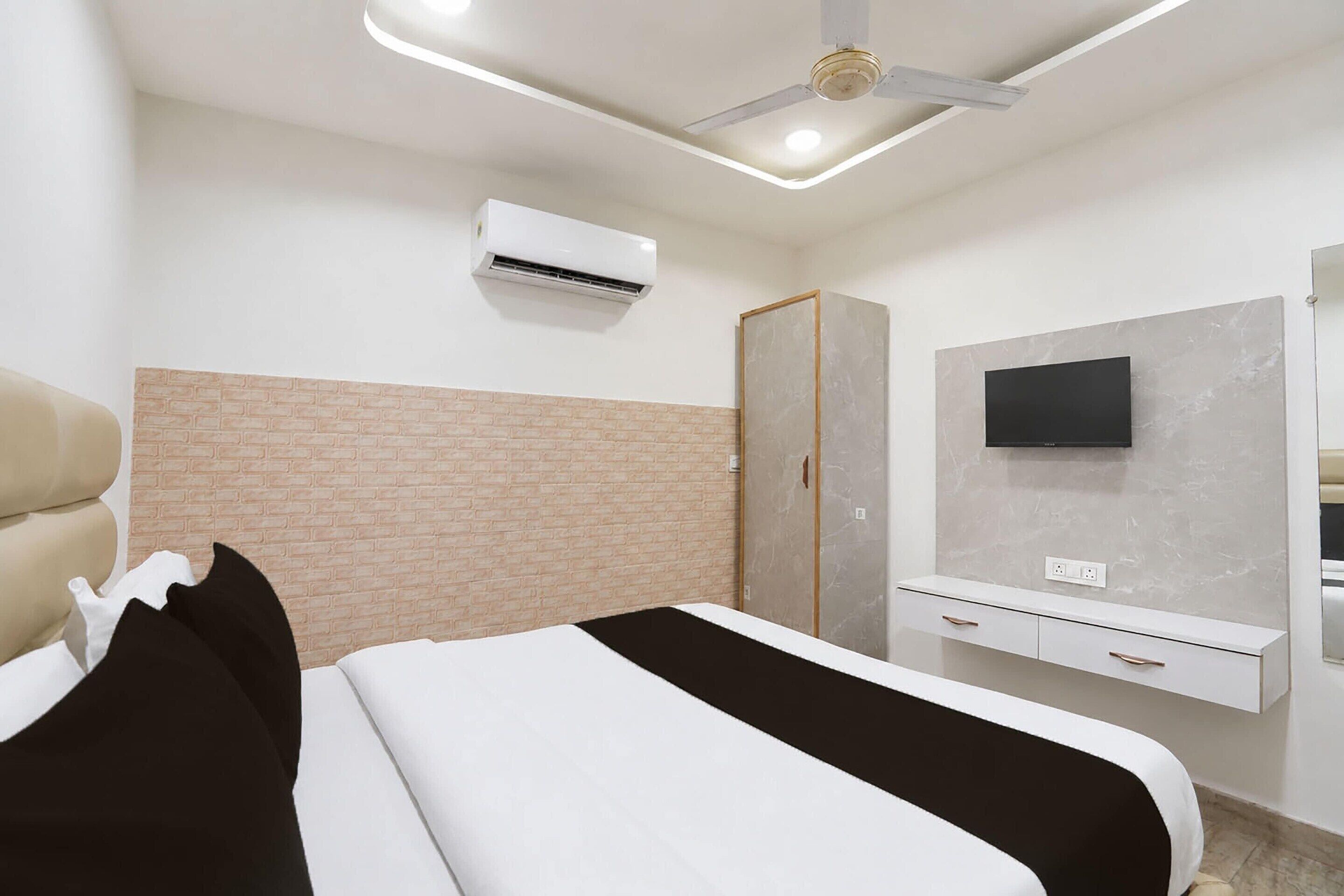 A hotel room with a bed, a TV mounted on the wall, a ceiling fan, and an air conditioning unit.